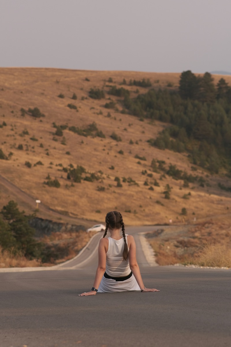 Woman sitting on a road looking toward a hill ahead